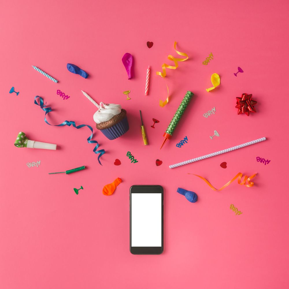Smartphone with colorful party items on pink background