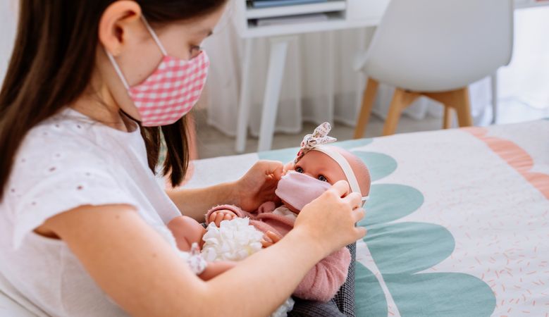 Girl with mask putting small mask on her doll