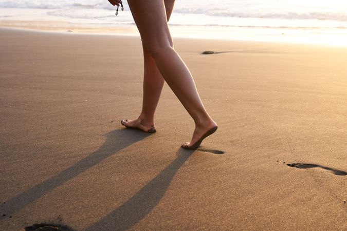 Crop woman strolling on sand of beach