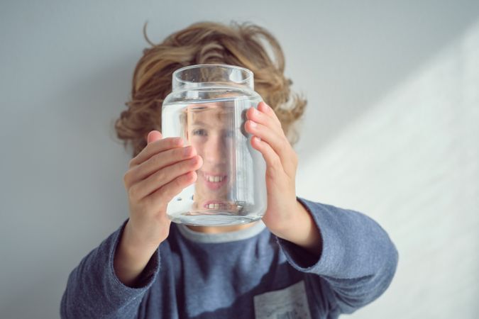 Smiling boy looking through glass jar