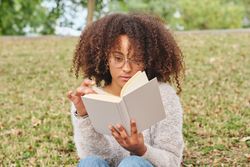 Black female flipping pages of book in nature