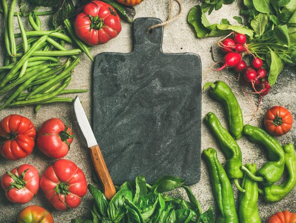 Fresh vegetables arranged with dark cutting board and knife in center