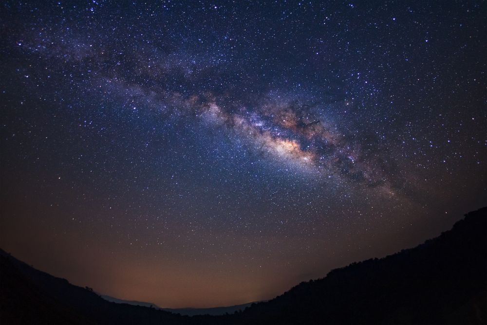 Landscape milky way galaxy with stars and silhouette of a standing happy man, Long exposure photograph, with grain.