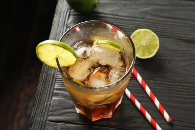 Glass of cold cola with citrus and ice on wooden table, space for text