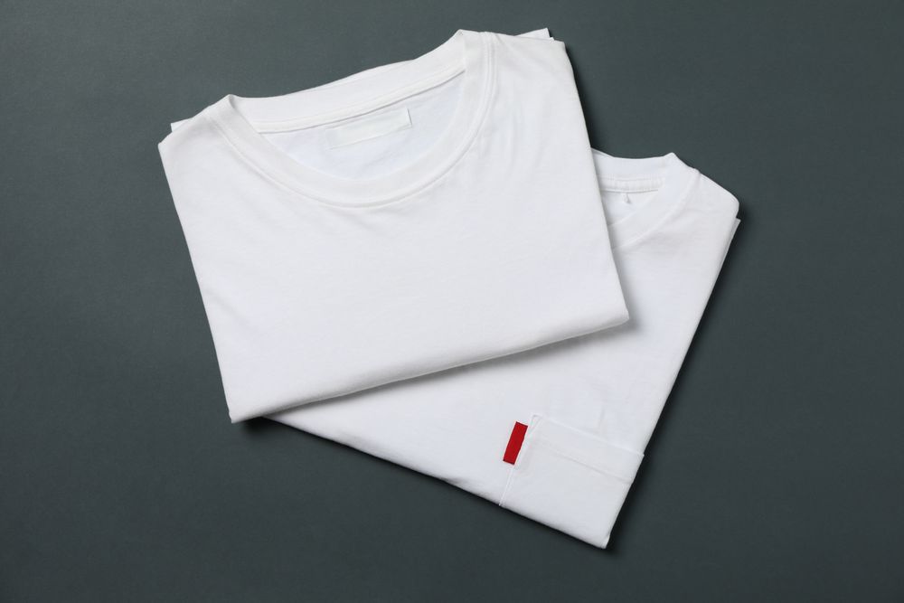Folded white t-shirts on light dark background, space for text