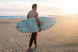 Man walking along beach with surfboard