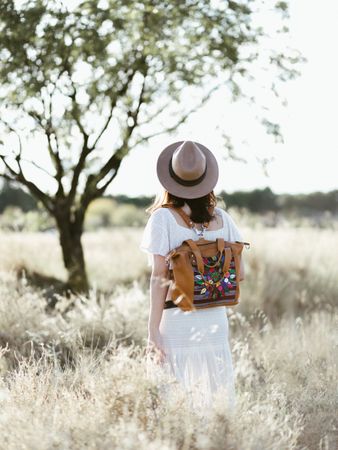 Female traveller with colorful backpack walking on field