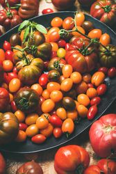 Assortment of different tomatoes in oval bowl, on wooden table, vertical composition, close up