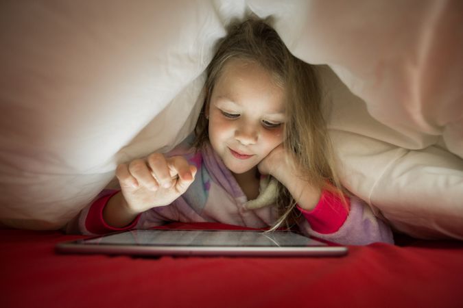 Girl using tablet under blanket