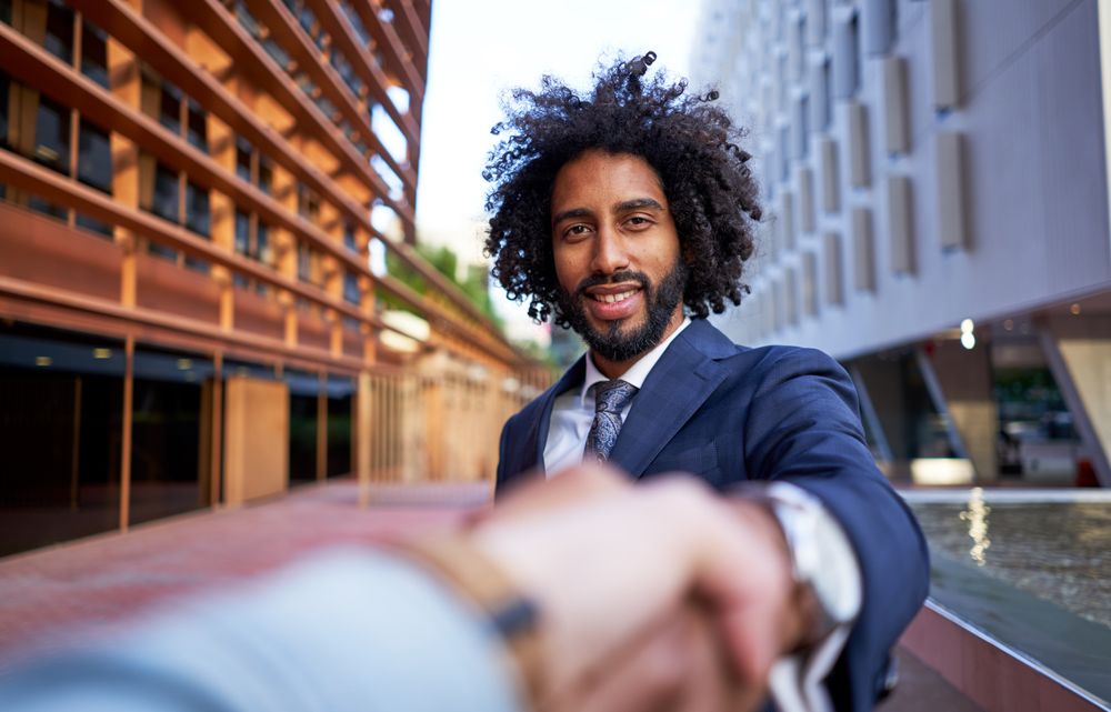 happy businessman shaking hands with partner and looking at camera
