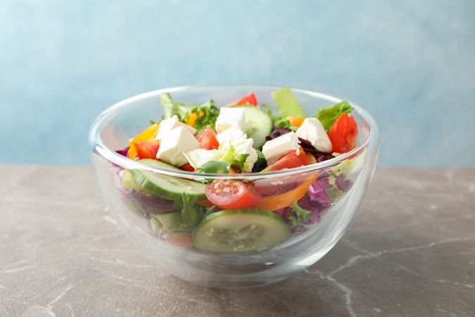 Glass bowl with fresh salad on grey background, copy space