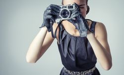 Model in vintage clothing and gloves taking picture with camera
