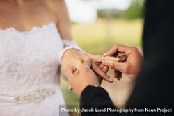 Closeup of couple exchanging wedding rings during their wedding ceremony outdoors 56KRN4