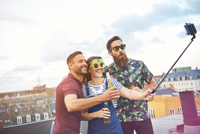 Group of friends with beer and funny glasses with selfie stick on rooftop