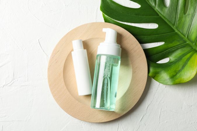 Palm leaf, wood plate, bottles with scrub and cream on plain background, copy space