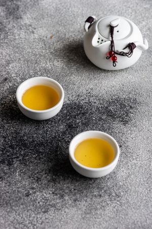 Cups of green tea and pot on grey counter