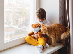 Toddler boy sits with teddy bear, both in medical masks