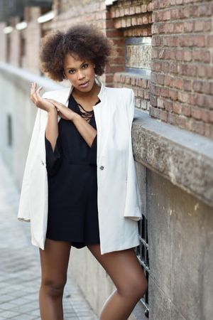Female in dress with blazer over shoulders standing next to outdoor wall, vertical