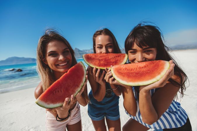 Three young women enjoying watermelon on seashore