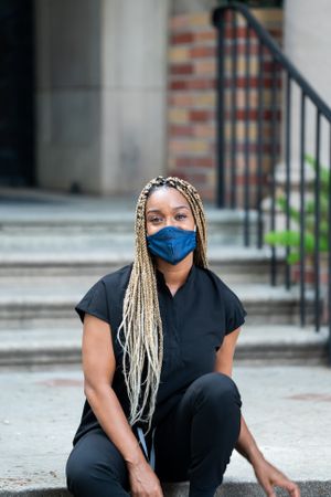 Portrait of healthcare worker sitting outside wearing scrubs and mask looking at camera