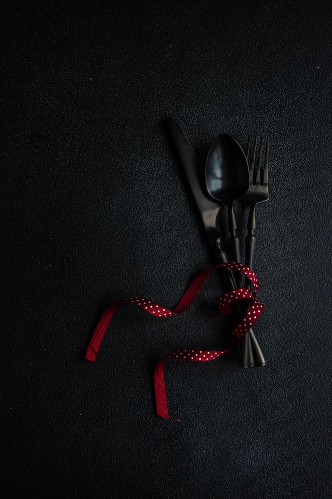 Dark cutlery on dark background tied with dotted red ribbon