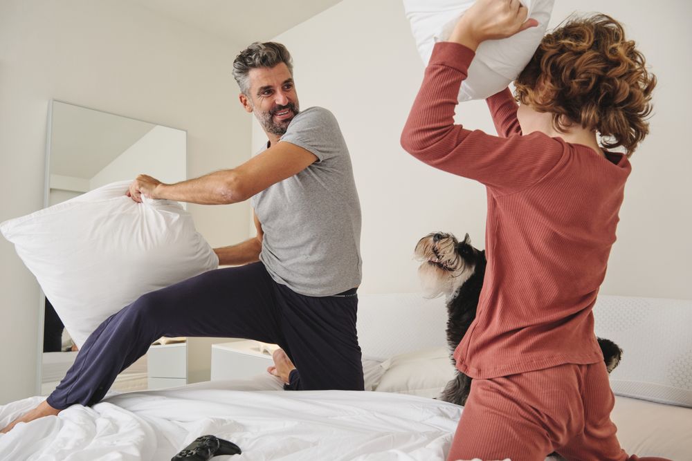 Happy man and boy fighting with pillows on bed