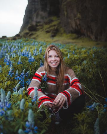 Portrait of smiling woman in brown and red sweater sitting in blue flower field