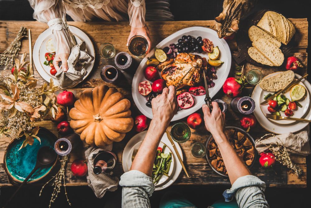 Autumnal table with squash and candles with man carving roast chicken and woman holding wine glass