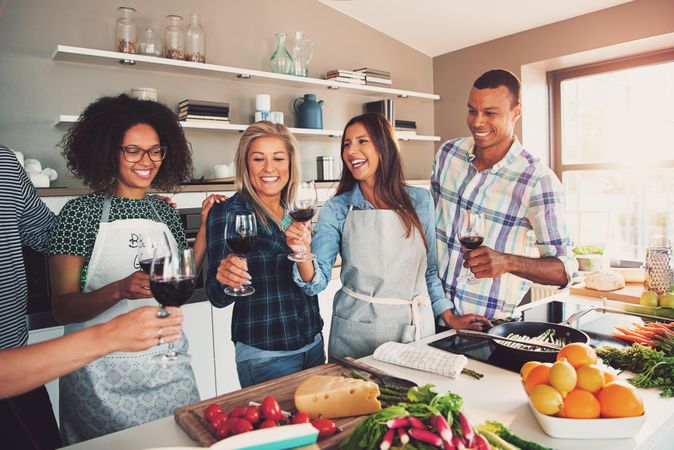 Friends toasting with red wine over a cutting board with cheese and vegetables