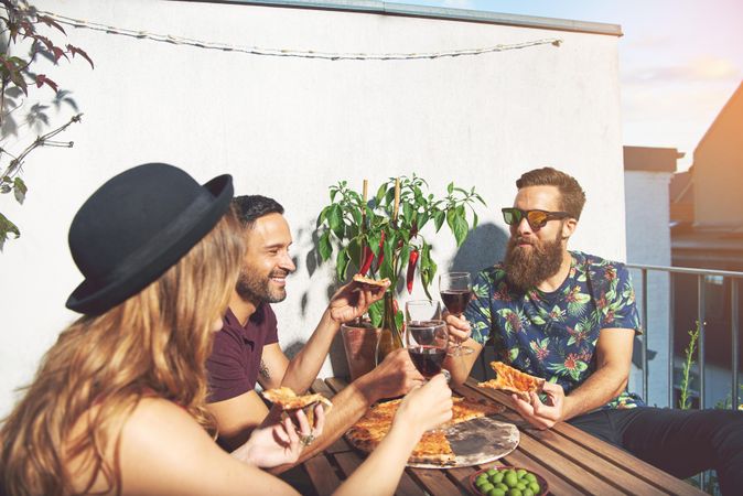 Group of friends on rooftop with red wine and eating pizza