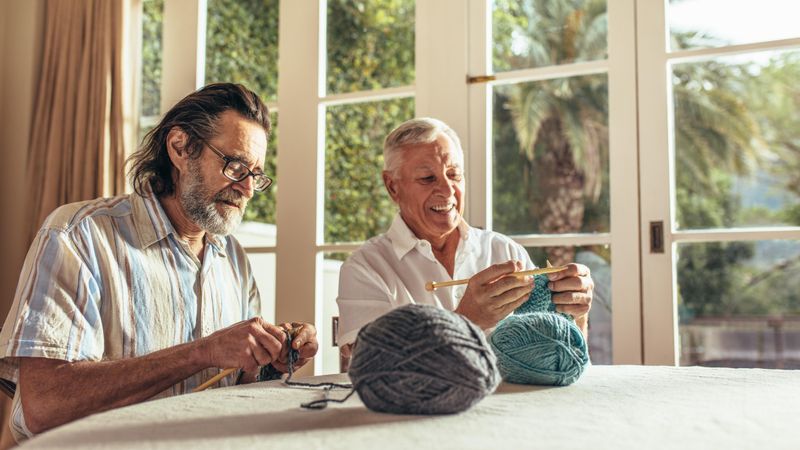 Older men sitting at home and knitting sweater with the knitting needles and woolen threads