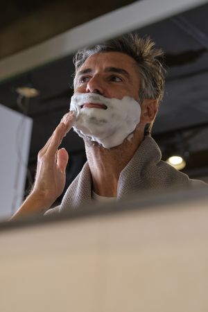 Happy male applying shaving foam in bathroom