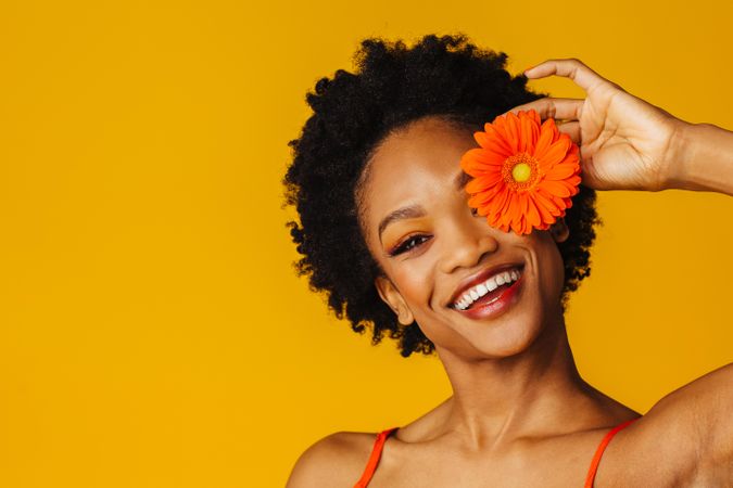 Joyful Black woman holding a flower over her eye
