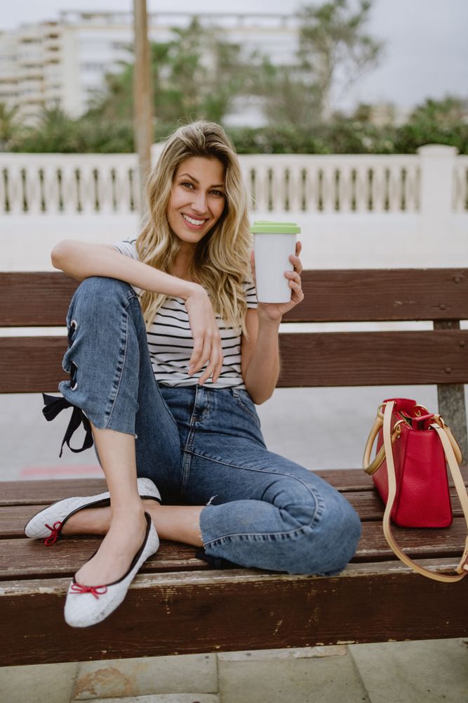 Happy woman with disposable cup of coffee sitting on street bench