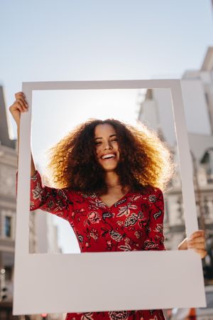 Beautiful woman holding a blank photo frame in hand and smiling at camera