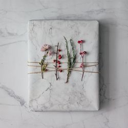 Marble wrapped present topped with winter foliage on marble background