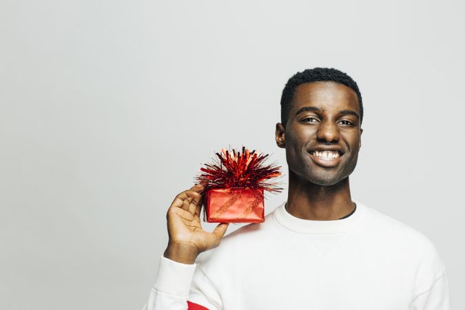Smiling Black man holding a present wrapped in red on his shoulder