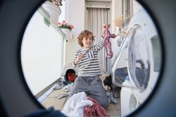 Boy sitting near washing machine and holding panties with disgus