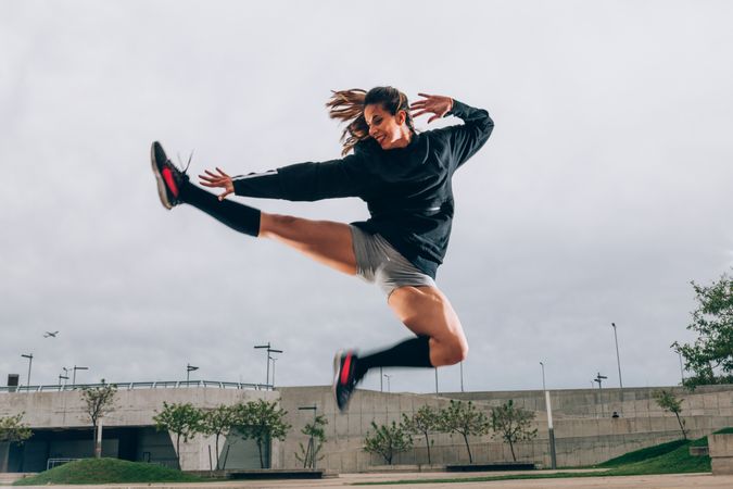 Female dancer in active wear smiling while dancing in jump outdoors