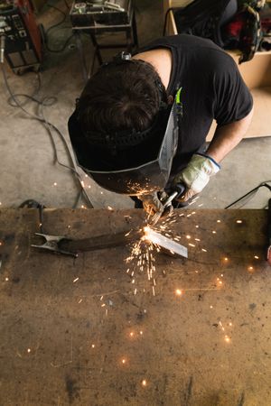 Welder in protective helmet welding metal detail in workshop