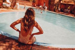 Back view of woman in brown bikini sitting on swimming pool side 5nowA4