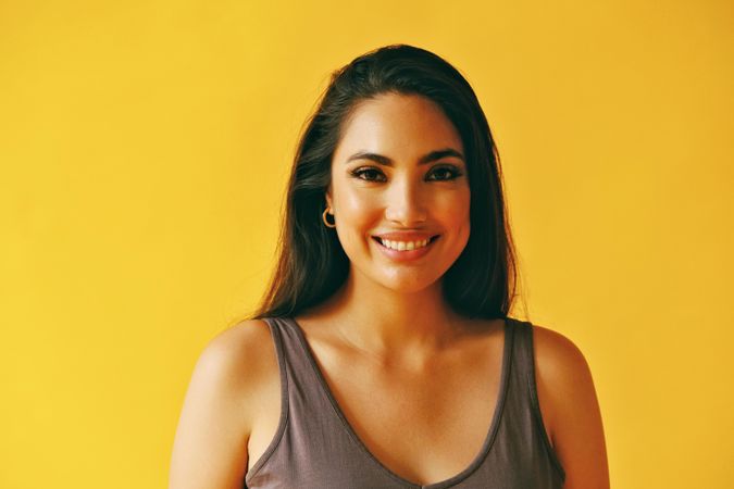 Headshot of smiling Hispanic woman looking at camera with yellow background, copy space