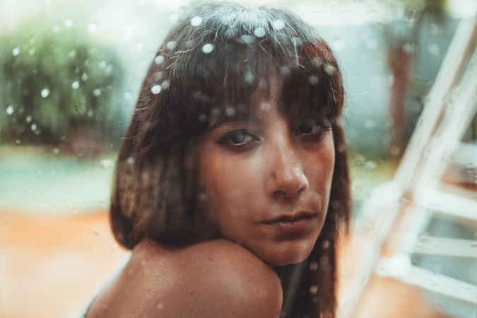 Woman looking at camera behind a wet glass
