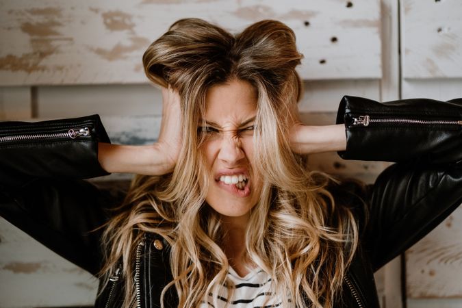Long haired woman clutching head and looking at camera with tension and anger