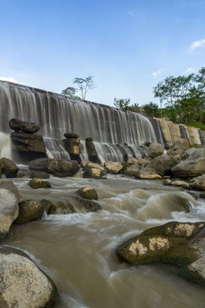 Waterfall and pile of stones in river with blue sky