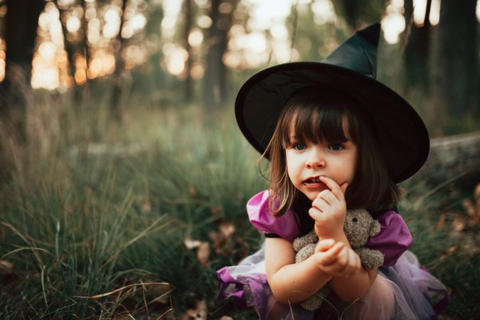 Close up of girl in witch costume crouched down in the forest with finger to her mouth
