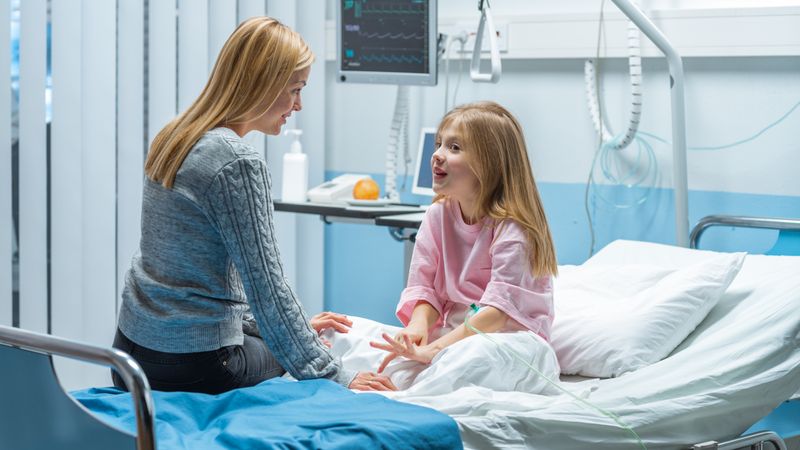 Healed Little Girl Sits on a Hospital Bed and Chats with Her Mother