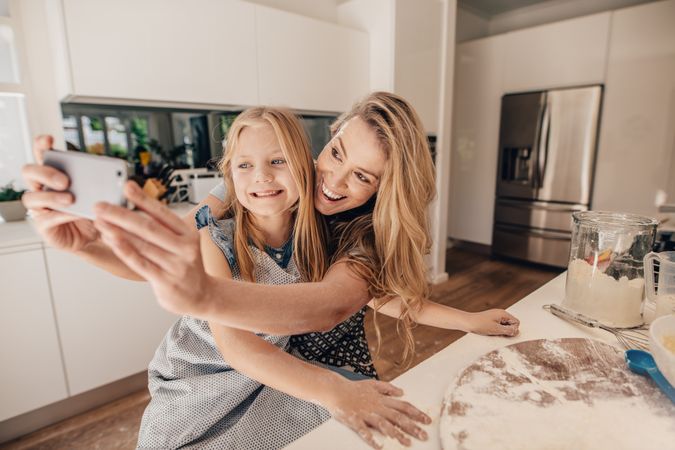 Happy mother and daughter taking selfie with mobile phone while cooking