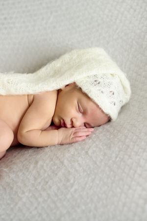 Close-up of a newborn baby girl, sleeping on a gray blanket and a white bonnet