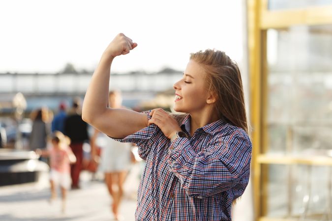 Smiling woman stands on the street curling her bicep